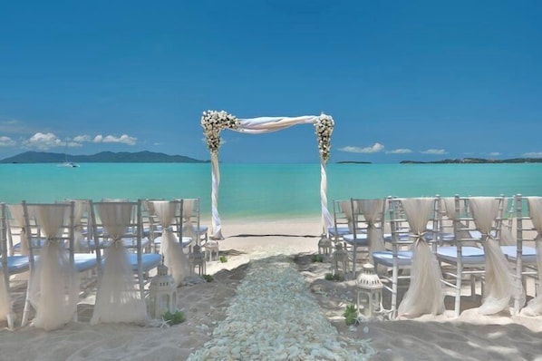 Decoración para una boda en la playa, con un arco blanco y sillas dispuestas para los invitados.