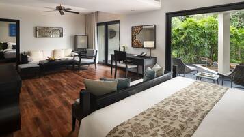 A modern hotel room with a large bed, a desk, a sofa, and a balcony with a view of greenery.