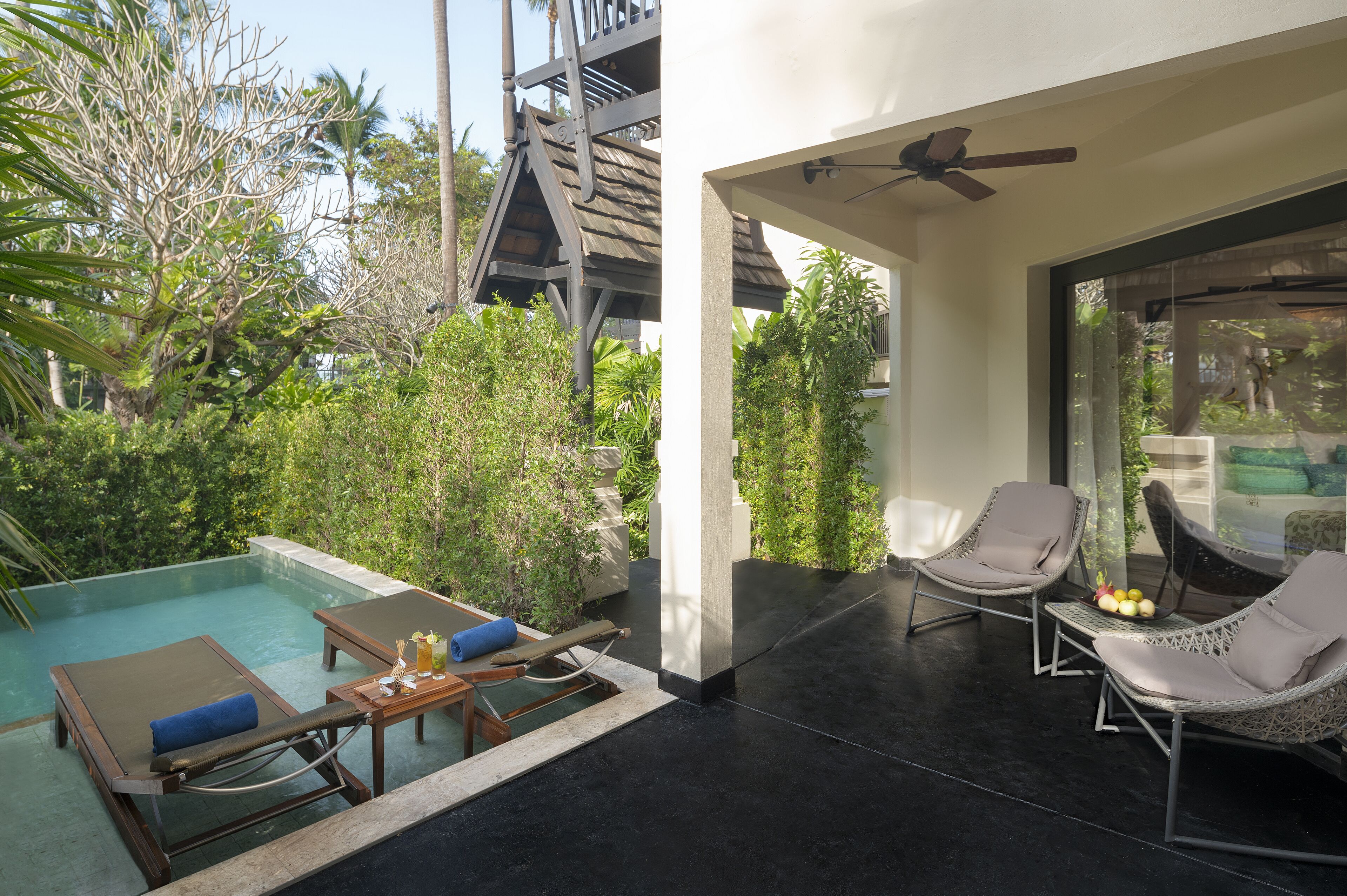 A pool area with lounge chairs and a table, surrounded by greenery and a modern building structure.