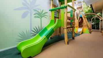 Un espace de jeux pour enfants avec un toboggan vert, un filet d’escalade et des structures de jeu en bois.