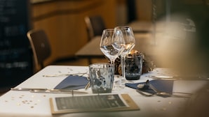 Een gedekte restauranttafel met wijnglazen, een menukaart en een kaars.