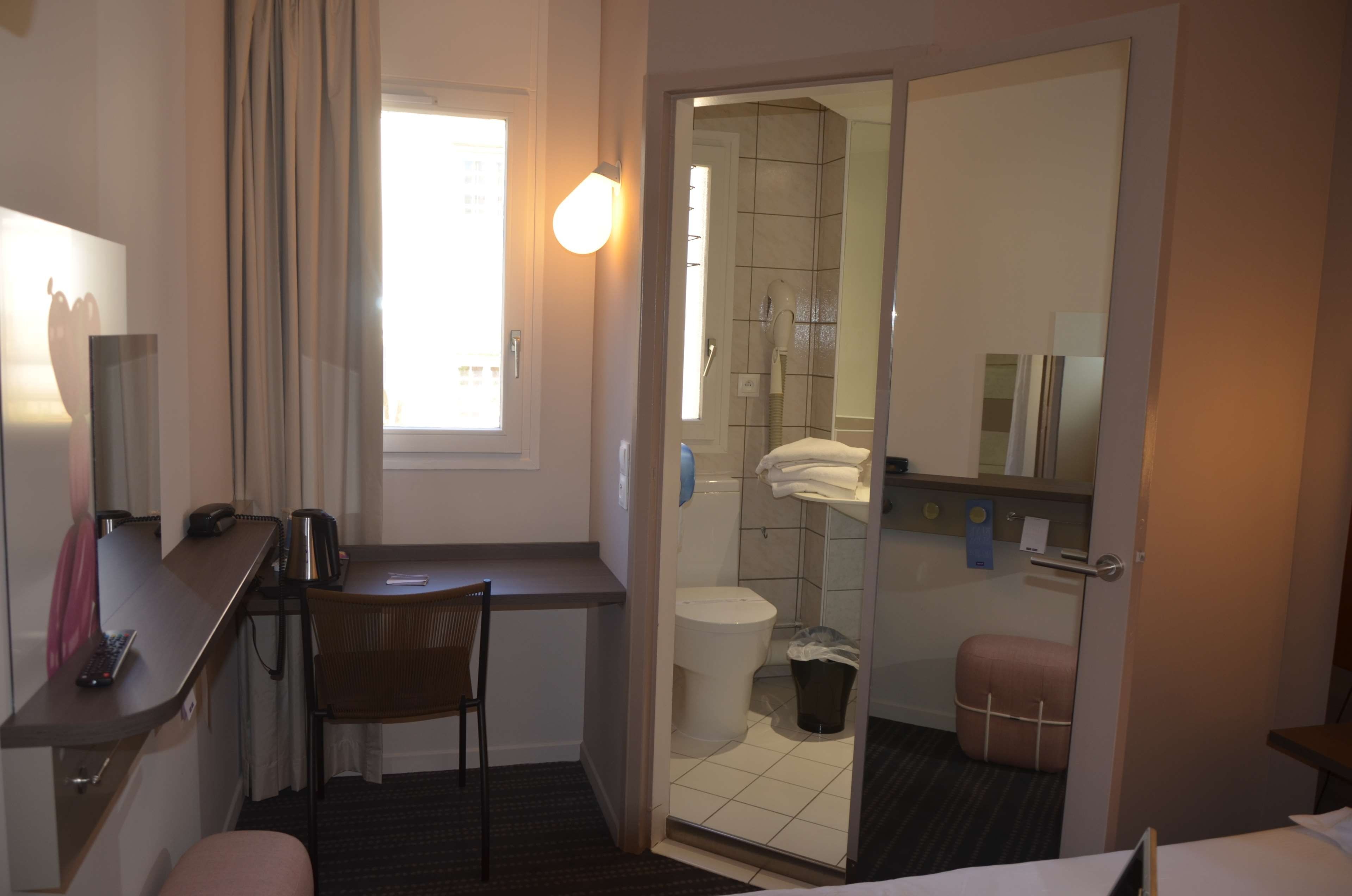 Habitación de hotel pequeña con escritorio, silla y un kitchenette.