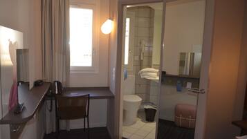 Habitación de hotel pequeña con escritorio, silla y un kitchenette.