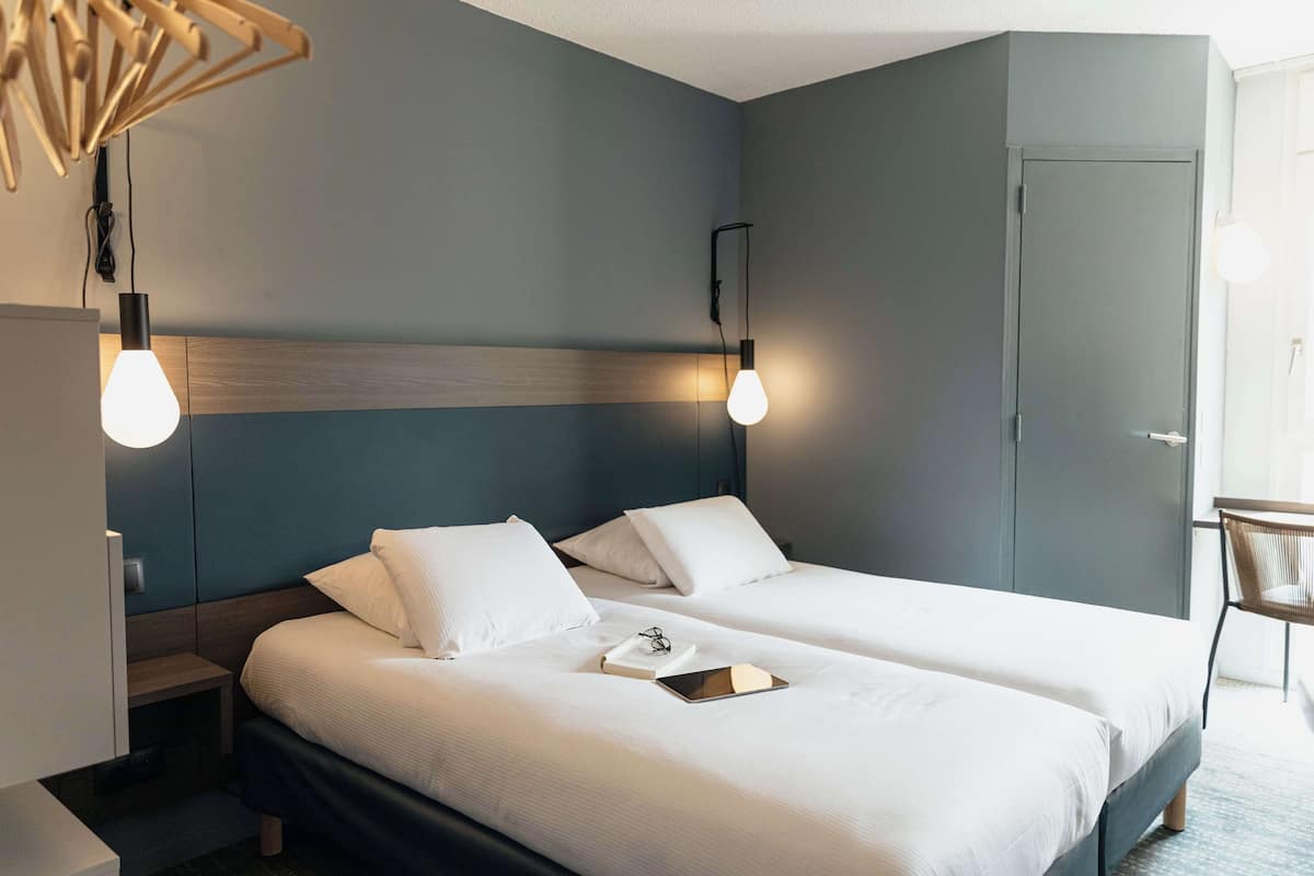 Una habitación de hotel con dos camas, una mesita de noche, una silla y un escritorio.