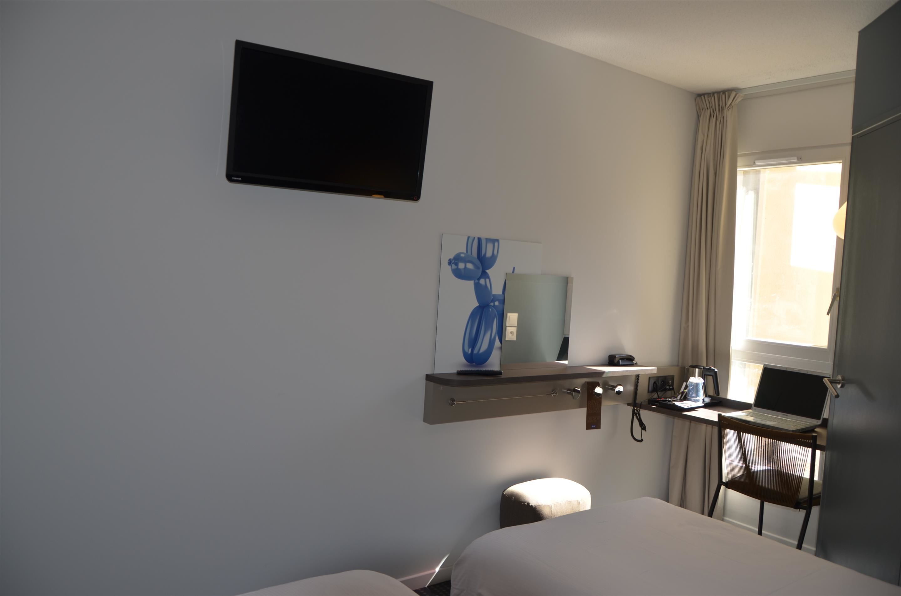 Una habitación de hotel con una cama, un escritorio con una computadora portátil, un televisor y una ventana con cortinas.