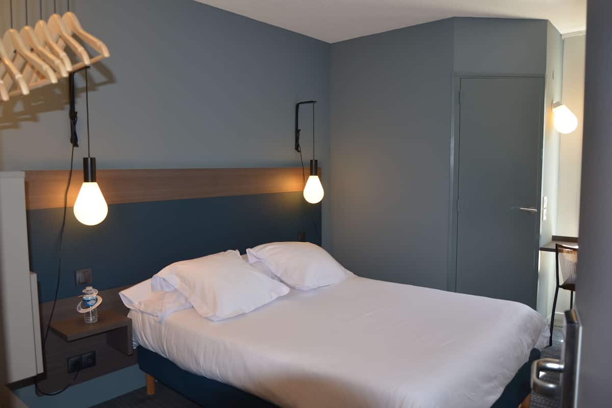 Una cama bien hecha con sábanas blancas, cabecera de madera y dos lámparas de noche.