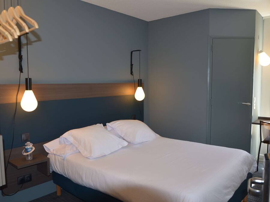 Een net opgemaakt bed met witte lakens, een houten hoofdbord en twee bedlampjes.