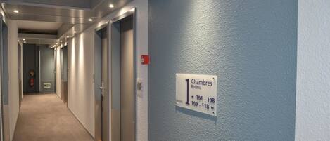 A hotel corridor with doors labeled "Chambres 1" and numbered 101-118.