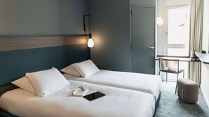 Een hotelkamer met twee bedden, een bureau, een stoel en een klein voetenbankje.