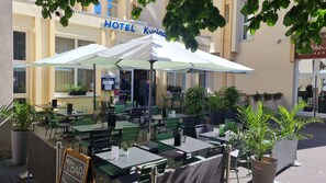 An outdoor seating area of a hotel with tables and chairs, some covered by umbrellas, and potted plants around. - Hotel Kyriad Metz Centre (Metz)