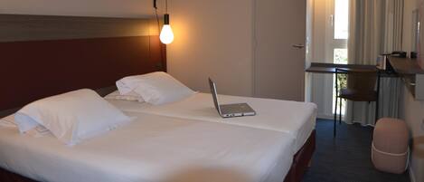 Habitación de hotel con dos camas, un escritorio, una computadora portátil, una silla y una ventana con cortinas.