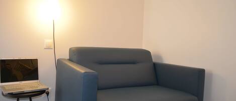 A modern room with a grey armchair, a small table with a laptop, and a wall-mounted light fixture.