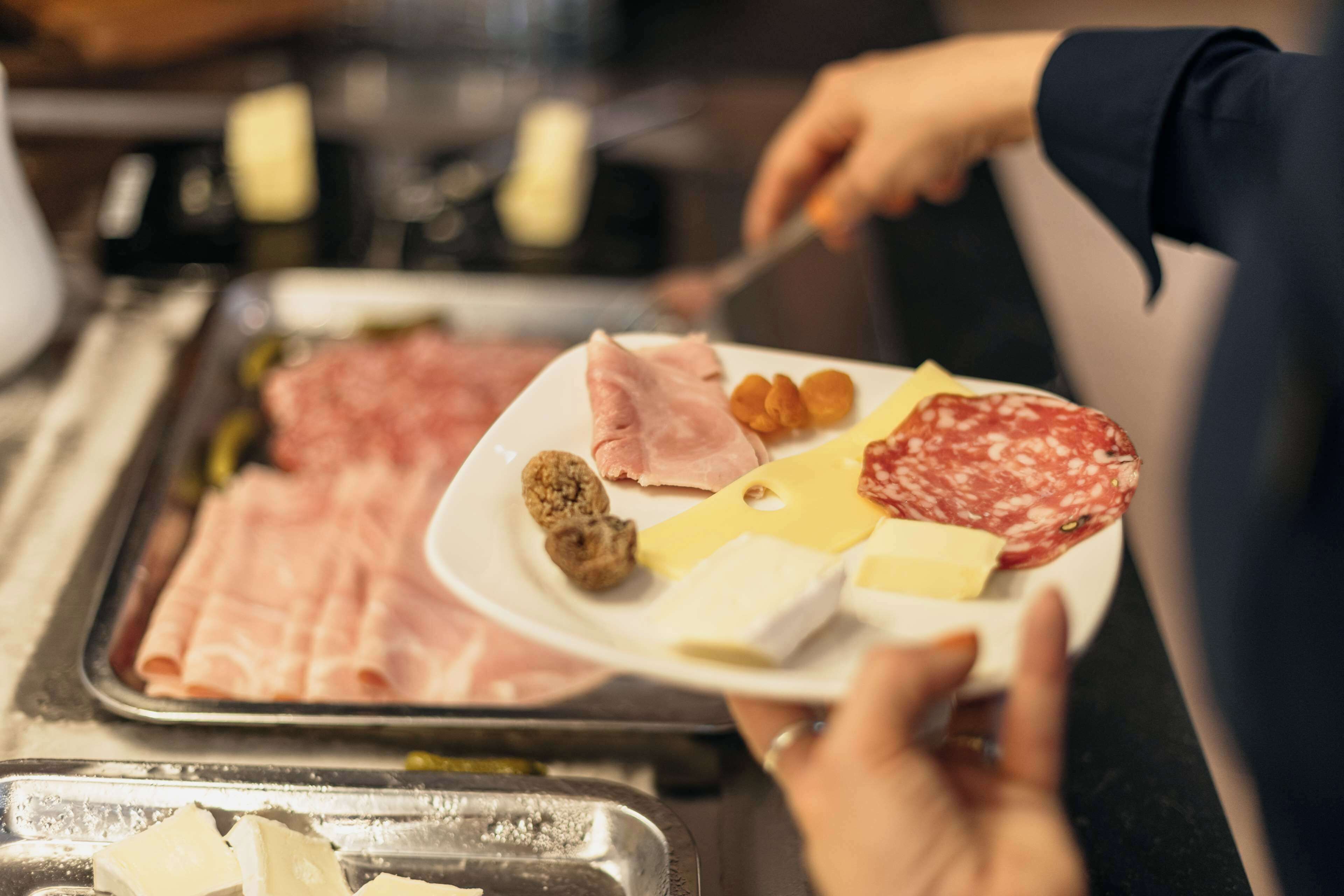 A person serving a plate with various cheeses, meats, and nuts.