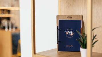 Une étagère en bois, sur laquelle se trouve un dossier bleu portant les inscriptions « MAOZE » et « RESTAURANT », le tout adossé à un mur blanc.