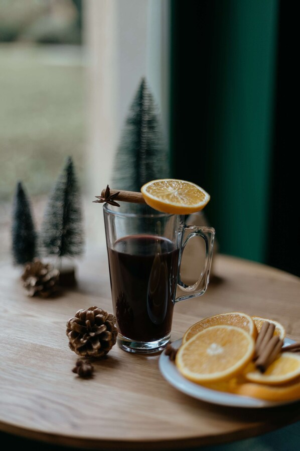 A glass mug with a dark liquid, garnished with an orange slice and cinnamon sticks, placed on a wooden table with pine cones and a plate of orange slices. - Hotel Kyriad Metz Centre (Metz)