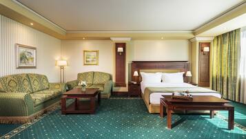 A hotel room with a large bed, two sofas, a coffee table, and a desk.