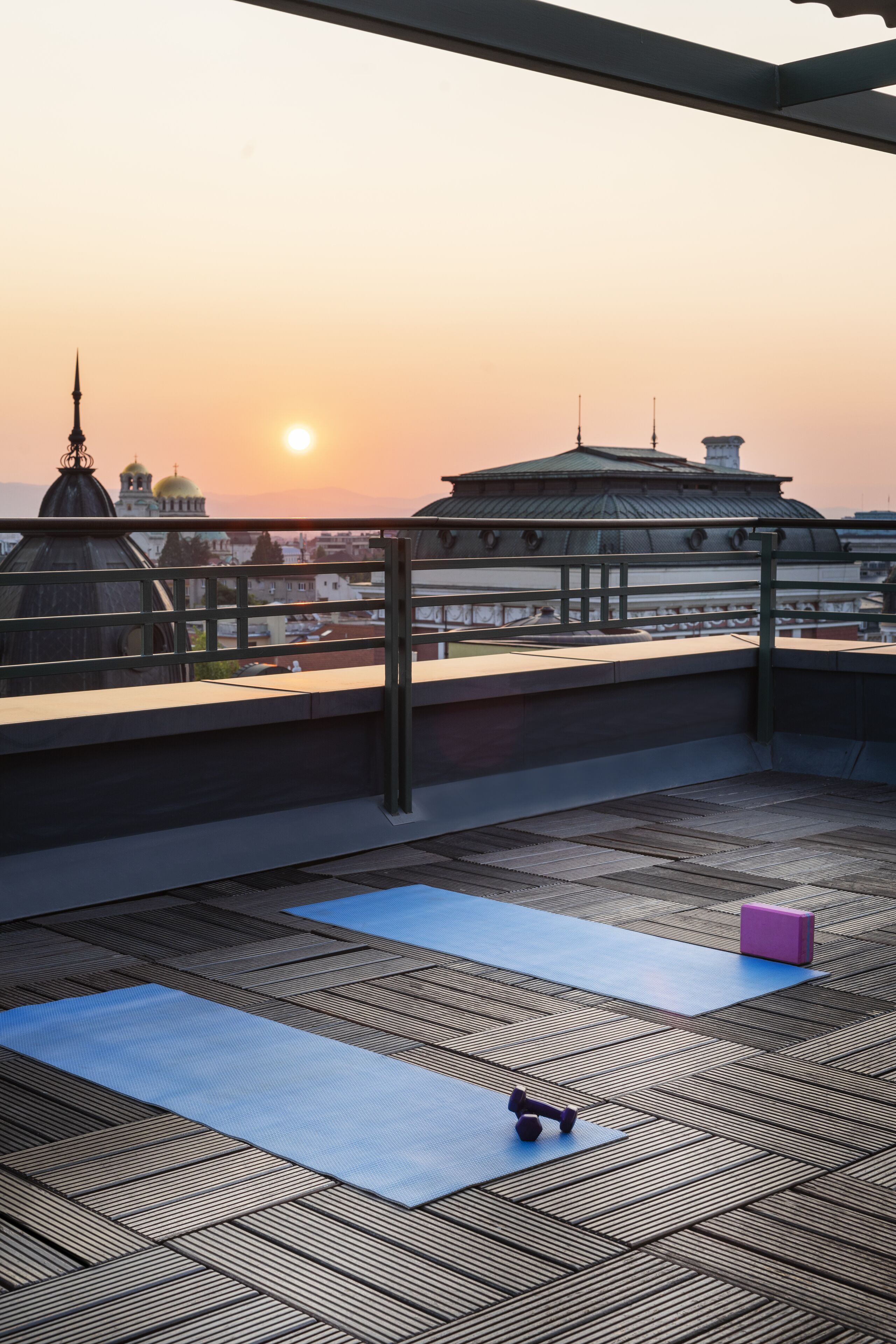 Una terraza en la azotea con colchonetas de ejercicio, un bloque rosa y mancuernas.