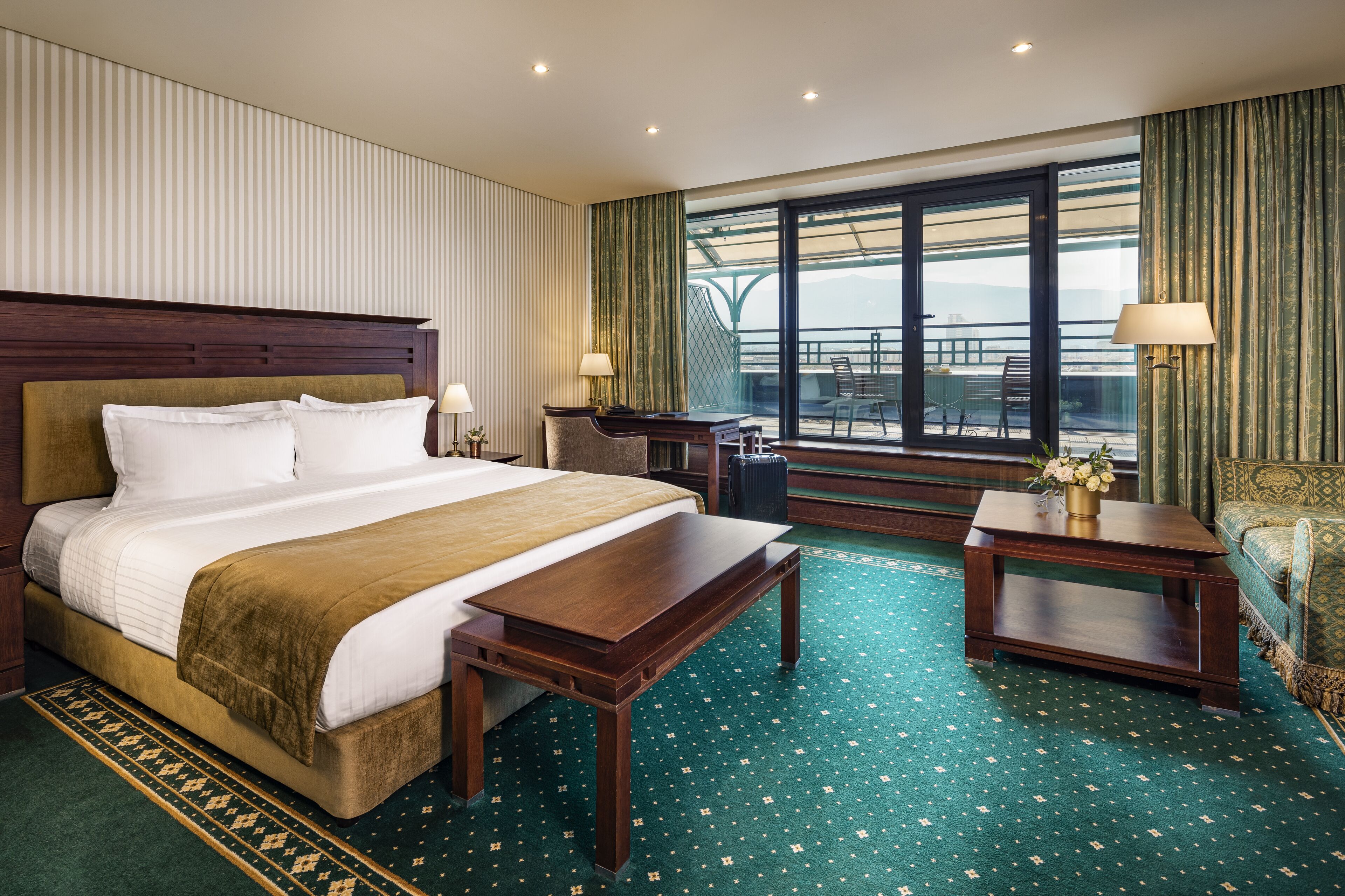 Habitación de hotel con una cama grande, un escritorio, una silla y vistas al exterior a través de un ventanal amplio.