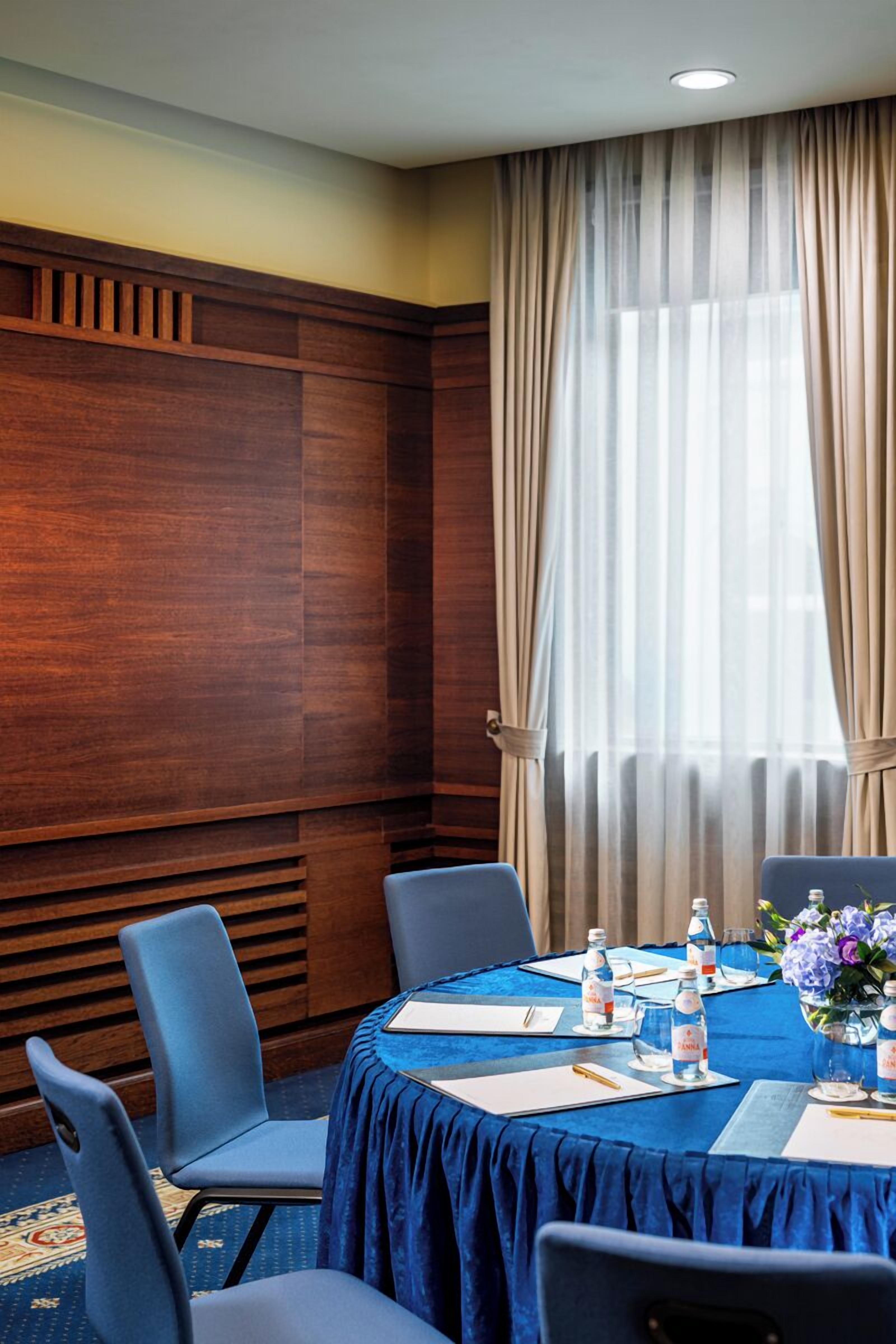 A conference room with a blue tablecloth, wooden paneling, and a large window with curtains.