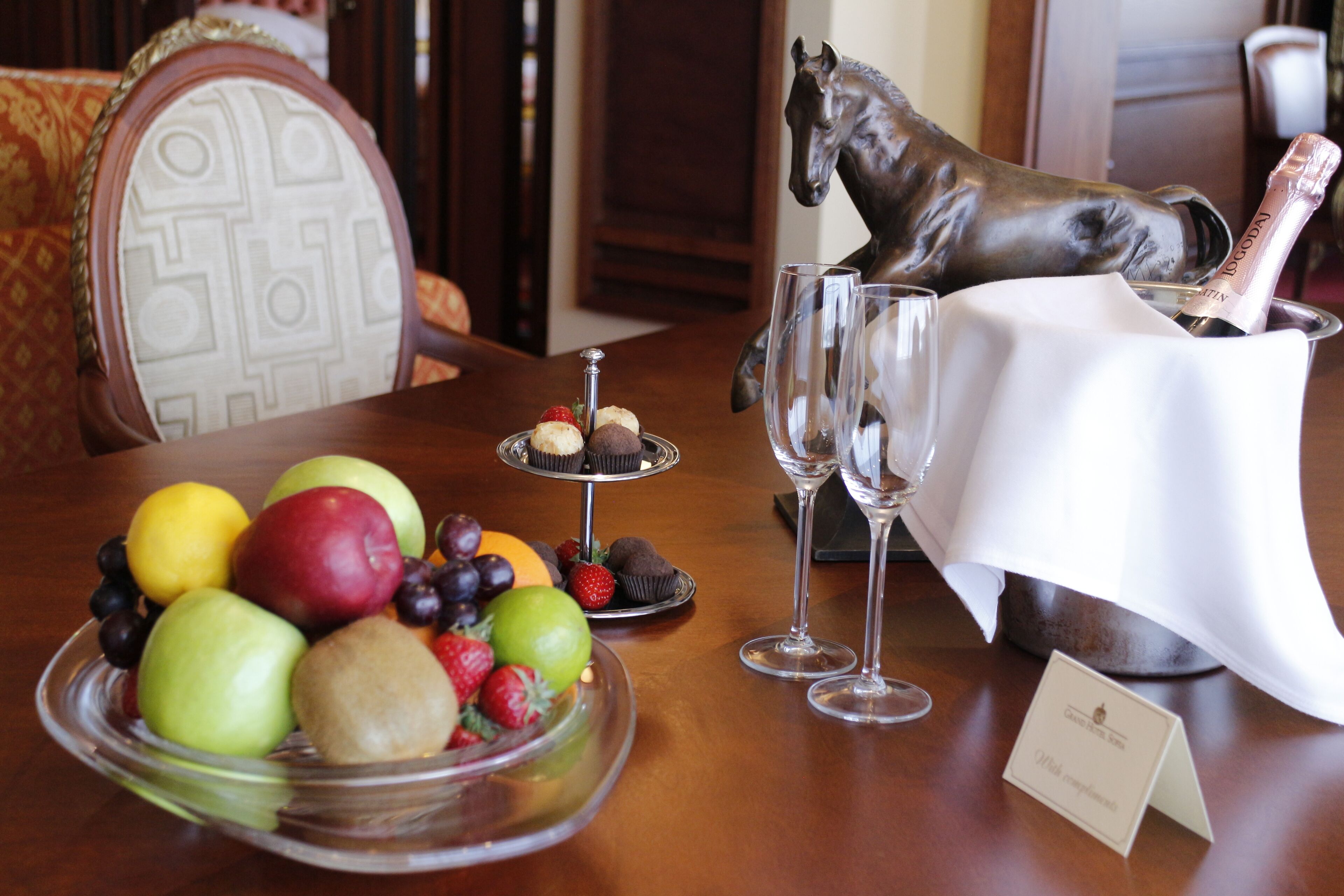 Een eettafel met een fruitschaal, champagneglazen en een paardenbeeld.