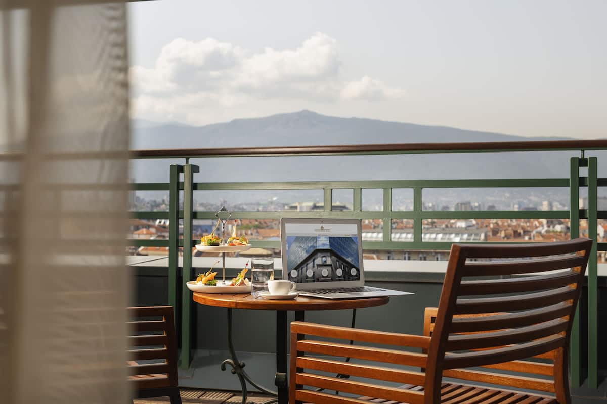 A balcony with a laptop, a cup, and a plate of food.
