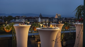 A rooftop terrace with tables set for dining, overlooking a cityscape with mountains in the background. - Grand Hotel Sofia (Sofia)