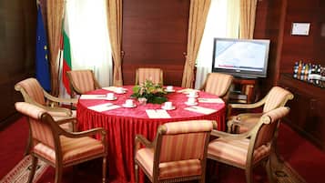 Un salón de conferencias con una mesa redonda, sillas, banderas, un televisor y una zona de bar.