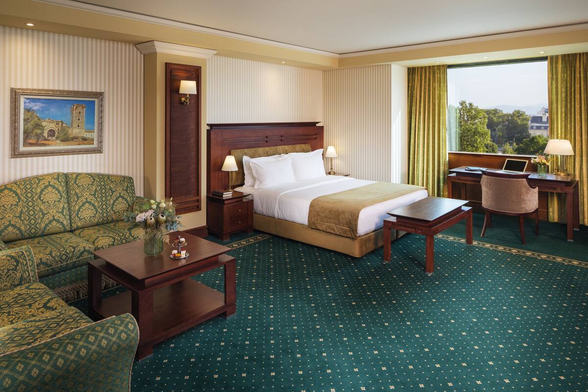 A hotel room with a large bed, a sofa, a desk, and a view of the city.