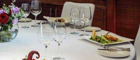 A round dining table set with white tablecloth, plates, cutlery, and wine glasses. A vase with flowers is on the table.