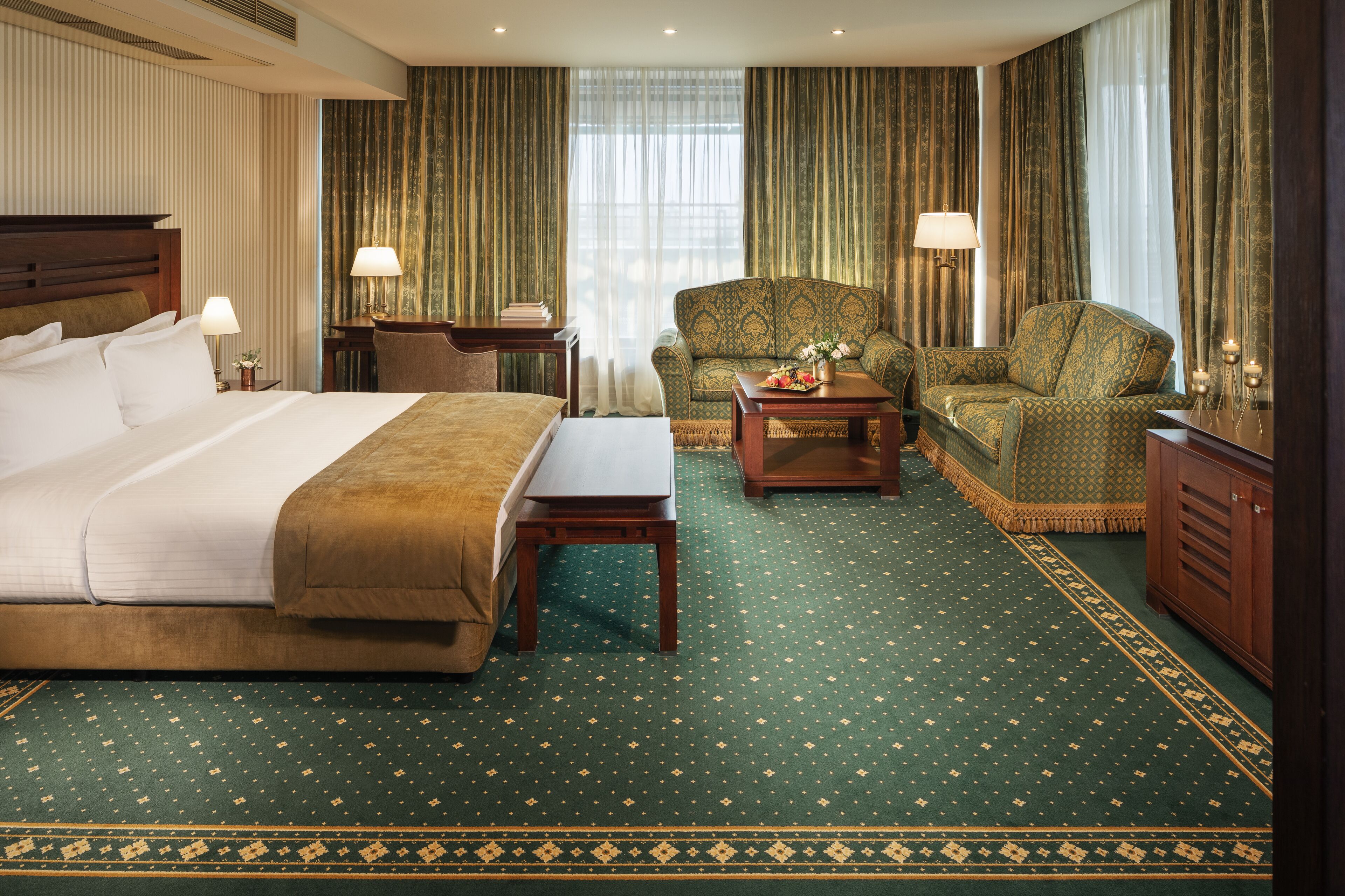 Habitación de hotel con una cama grande, dos sillones, una mesita y un escritorio con lámpara.