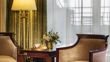 A hotel room with a wooden table, two armchairs, a lamp, a vase with flowers, a tray with a cup and a glass of orange juice.