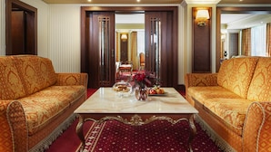 A hotel room with two patterned sofas facing a marble coffee table, a red carpet, and a mirror reflecting the room. - Grand Hotel Sofia (Sofia)
