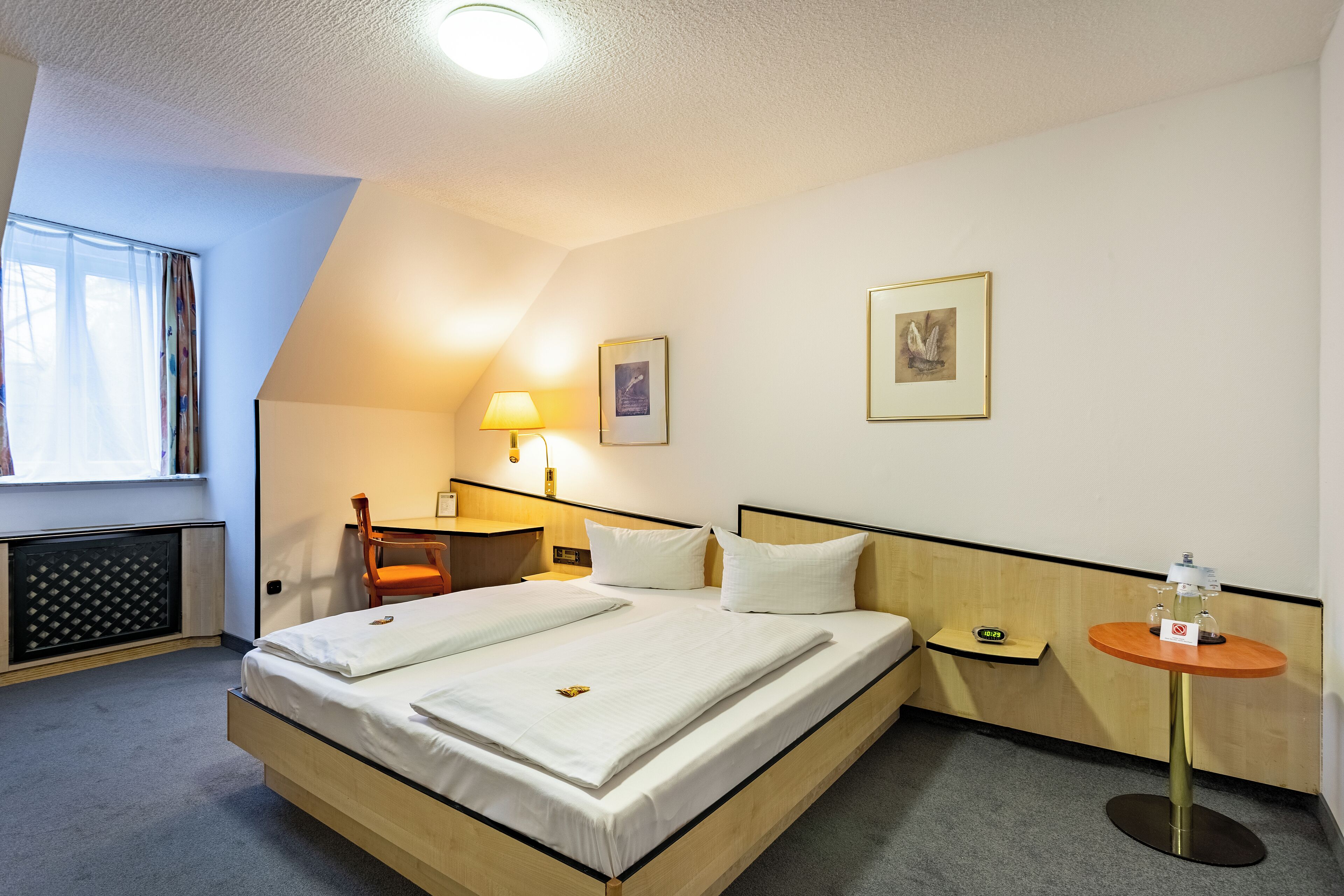 Ein Hotelzimmer mit einem großen Bett, einem Nachttisch, einem Sessel, einer Lampe und einem kleinen Tisch mit einer Flasche.
