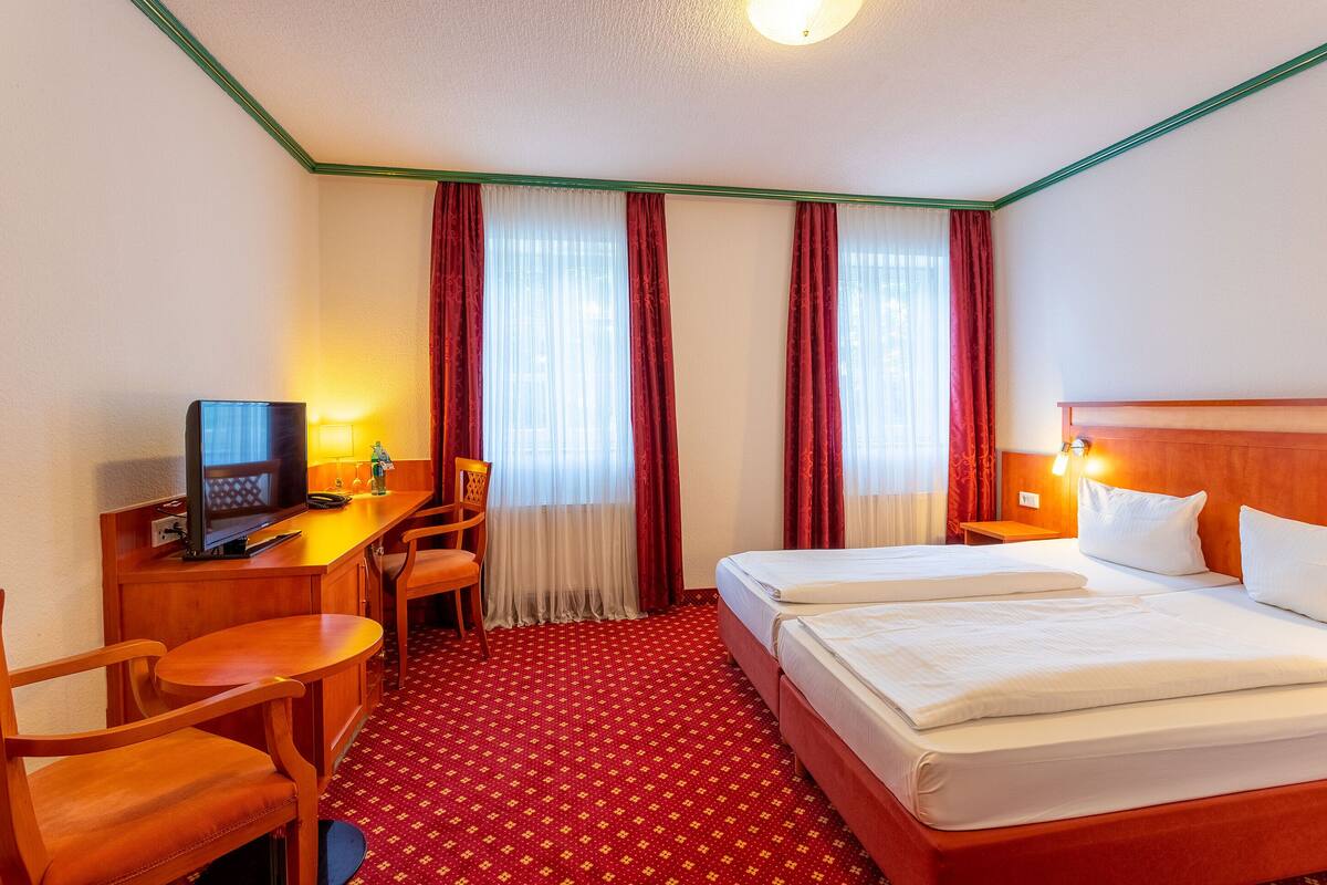 Una camera d'albergo con un letto, una scrivania con un computer, una sedia e una televisione.