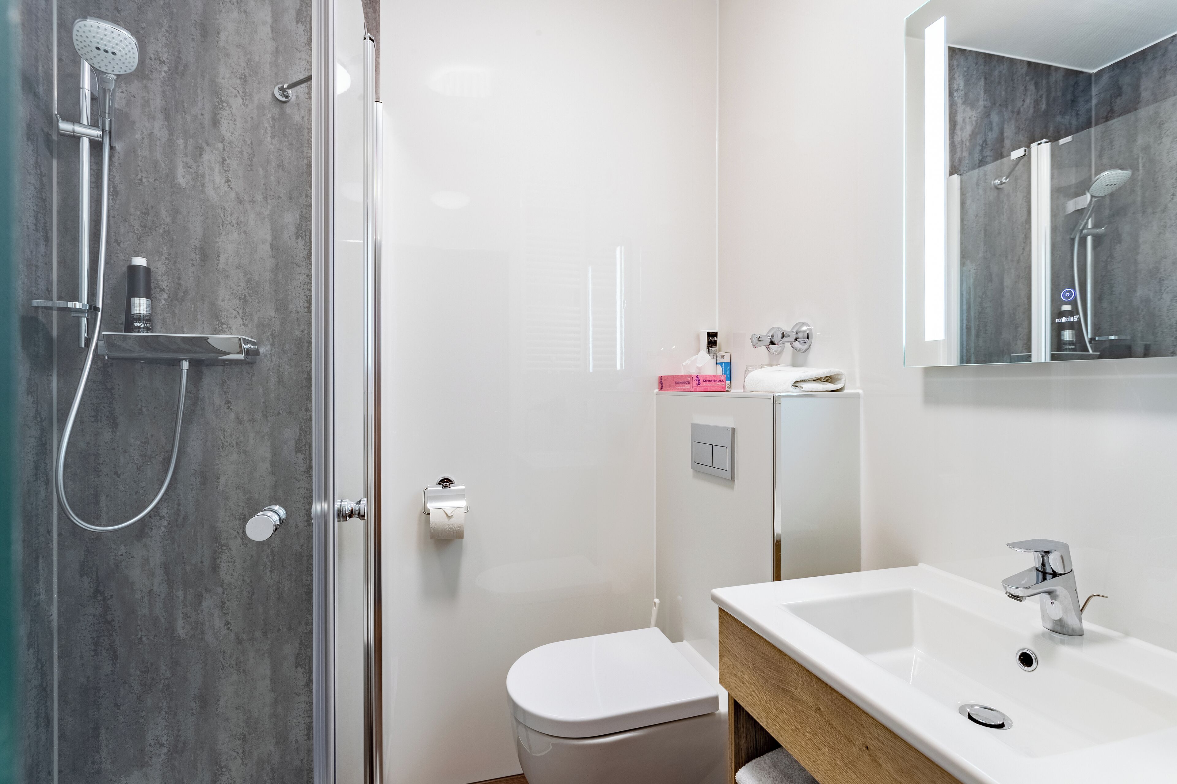 Ein modernes Badezimmer mit Duschkabine aus Glas, einer weißen Toilette und einem Waschbecken mit Holzablagefläche.