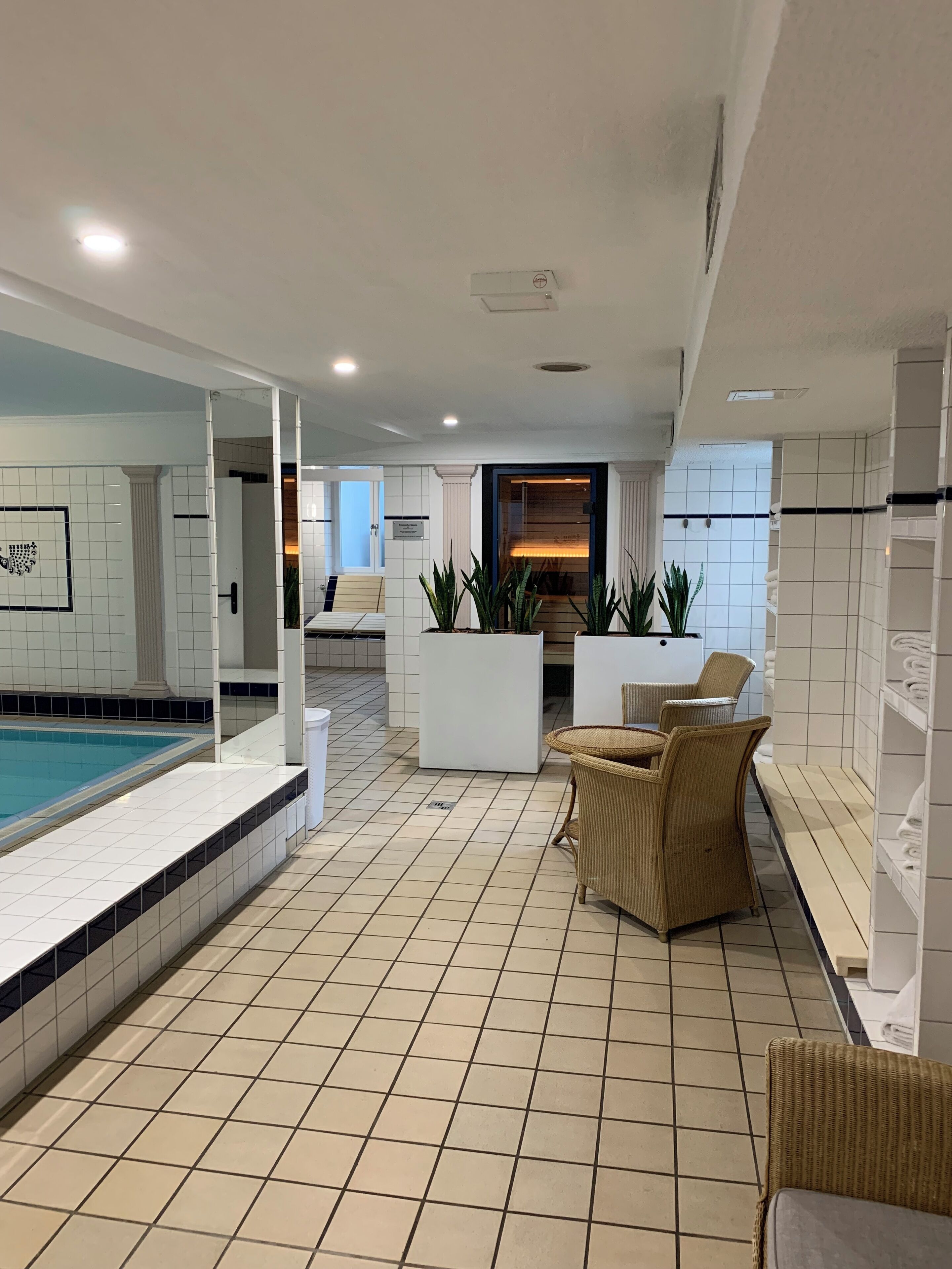 Uma área interna de piscina moderna, com piso ladrilhado, um espaço de estar com cadeiras de vime e um balcão de recepção.