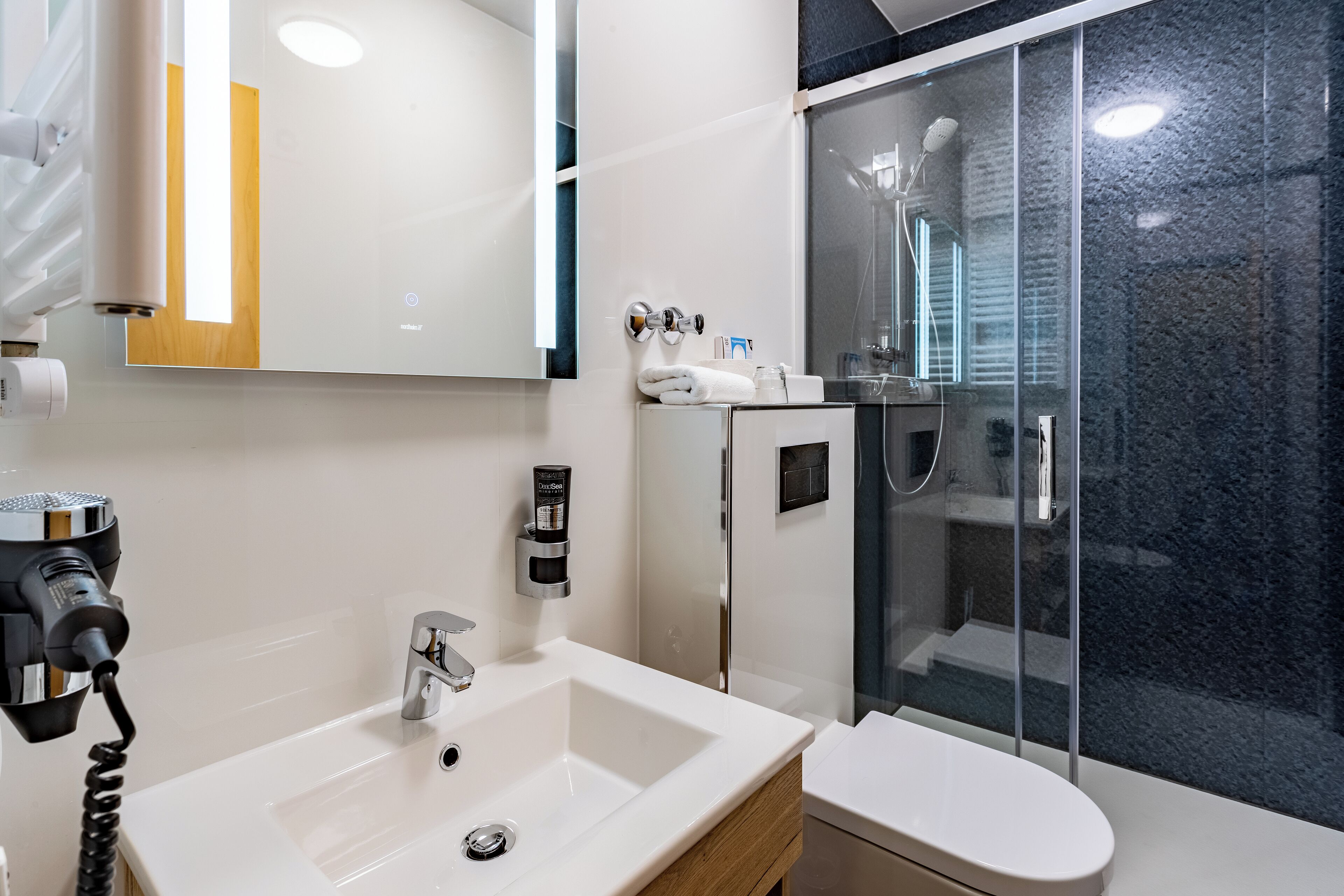Un baño moderno con un lavabo blanco, un inodoro, una cabina de ducha con mampara de vidrio y un espejo.