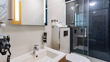 Un baño moderno con un lavabo blanco, un inodoro, una cabina de ducha con mampara de vidrio y un espejo.