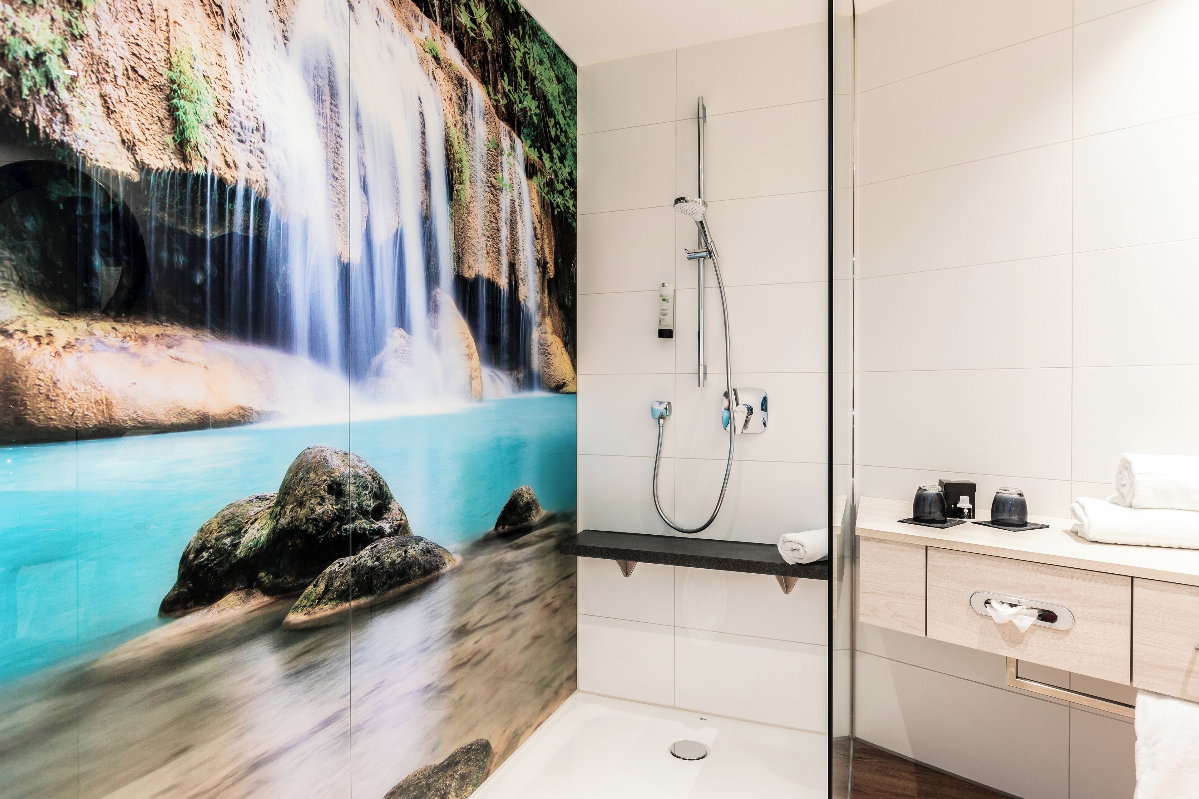 A bathroom with a waterfall mural, a shower, and a vanity with a towel rack.
