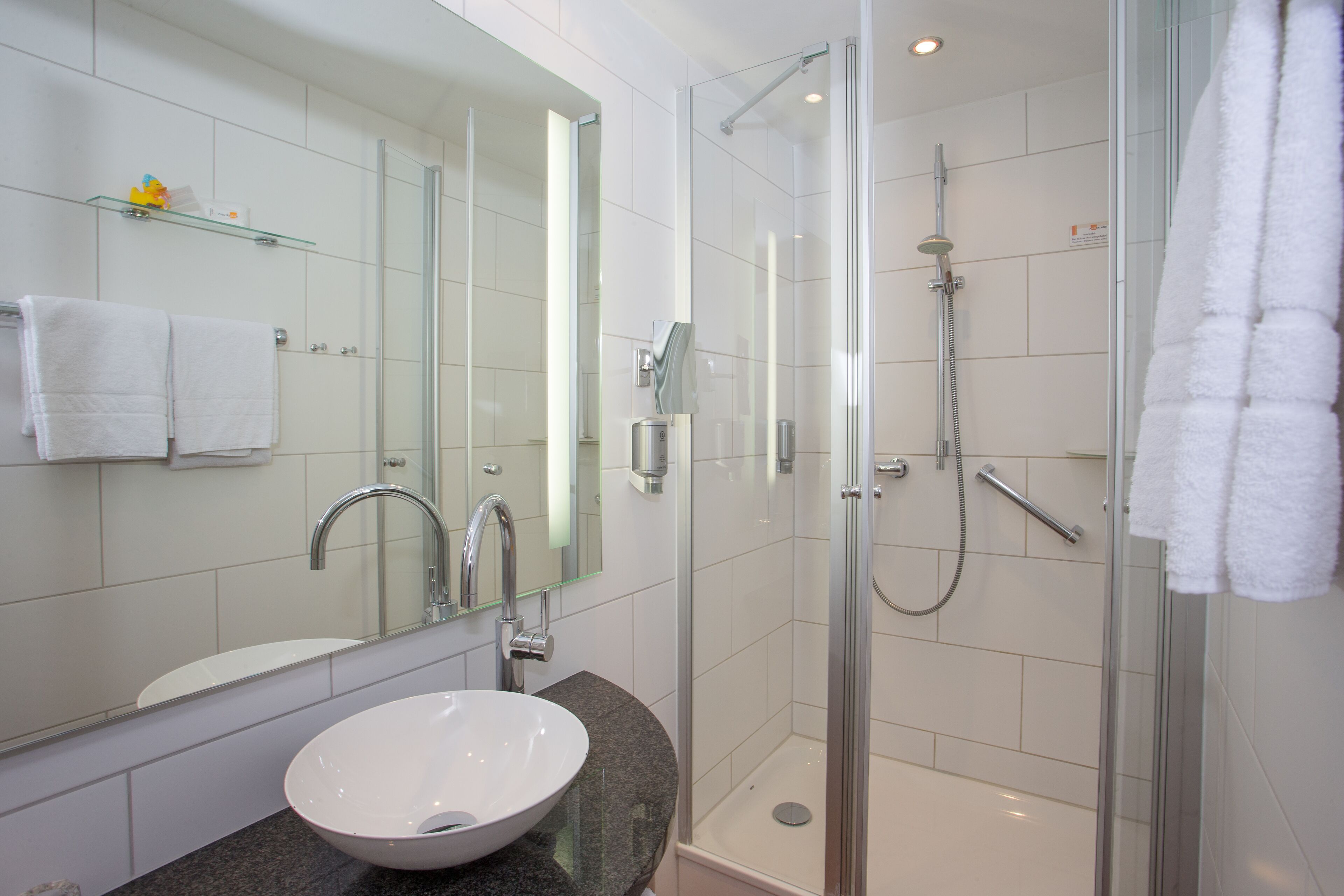 Un baño moderno con ducha de vidrio, un lavamanos blanco y un espejo grande.