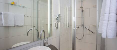 Un baño moderno con ducha de vidrio, un lavamanos blanco y un espejo grande.