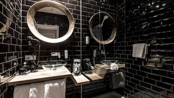 A modern bathroom with black tiled walls, two round mirrors, and a glass bowl sink.