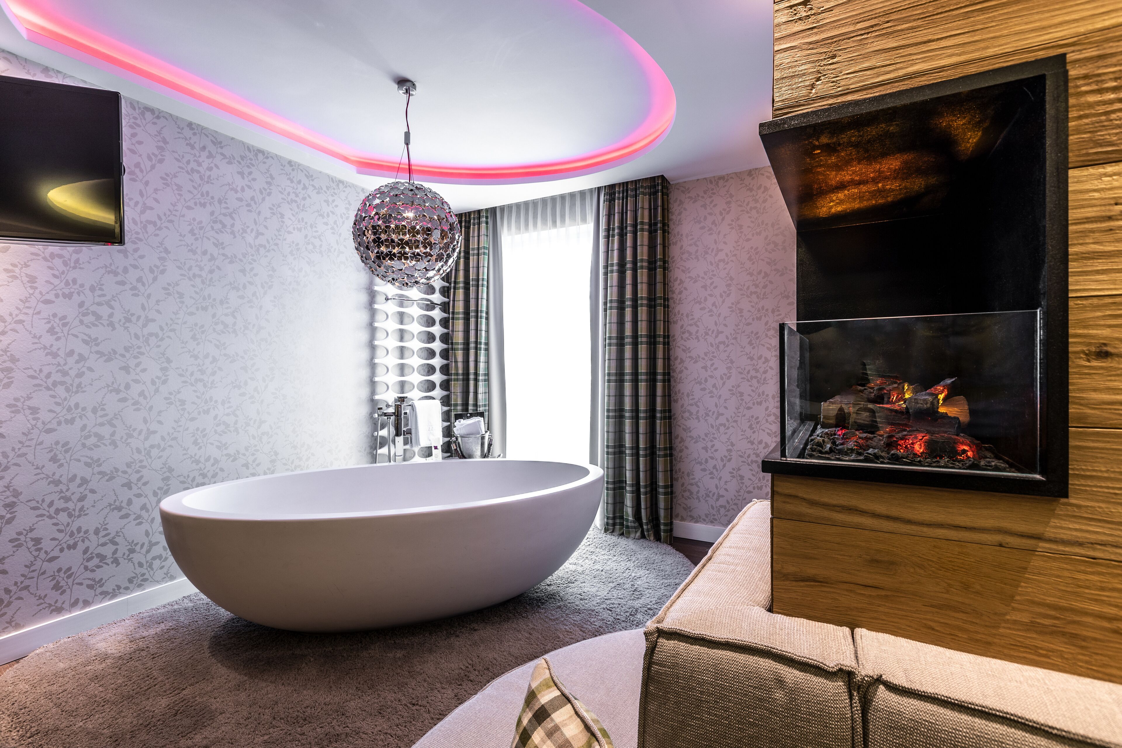 A modern bathroom with a freestanding bathtub, a decorative disco ball, and a built-in fireplace.