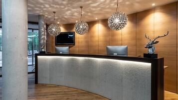 A reception desk with a curved design, a mounted television, and decorative crystal chandeliers.
