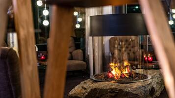 Un ambiente cálido y acogedor con una chimenea central, una lámpara moderna e iluminación ambiental.