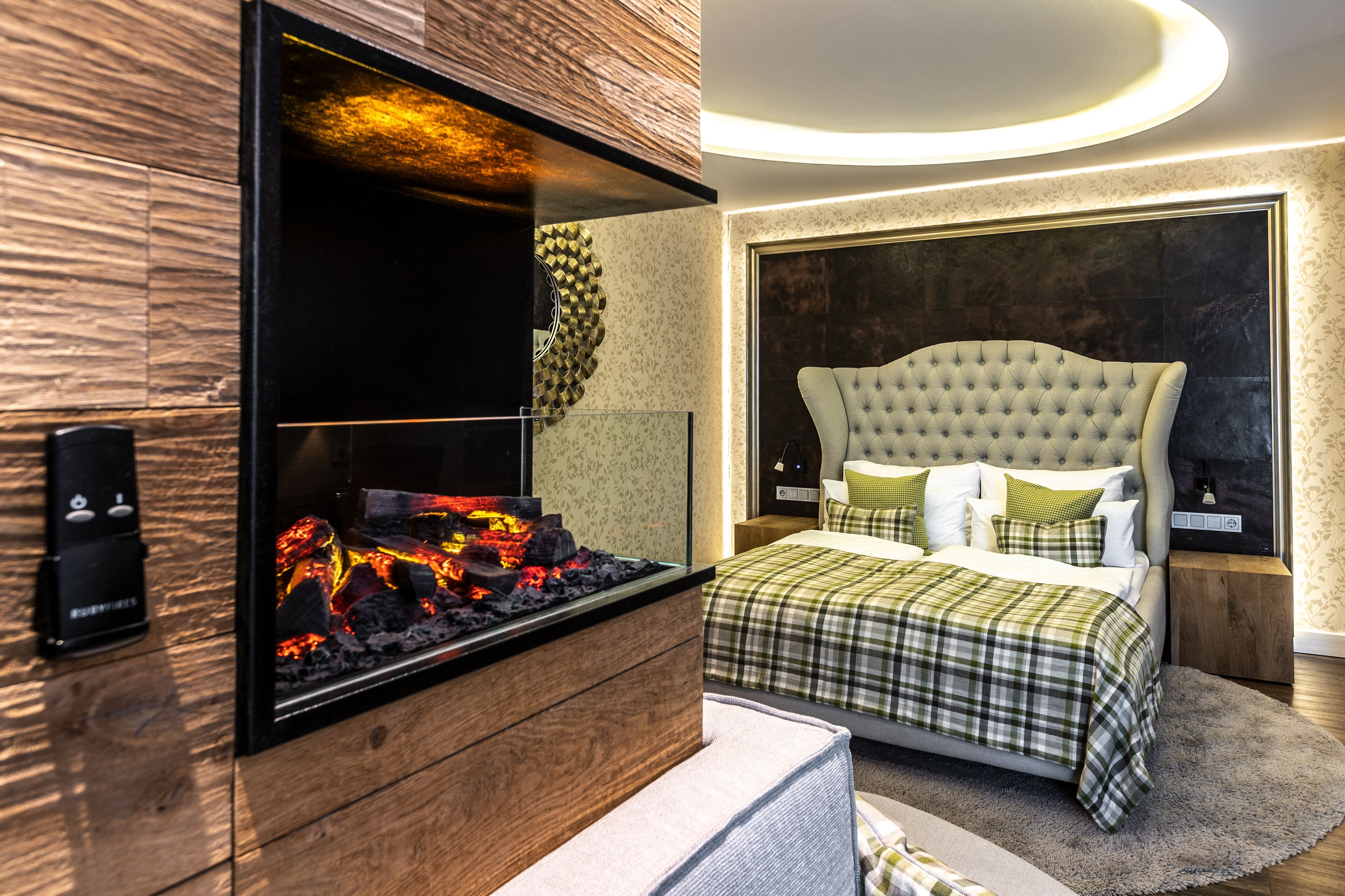 Une chambre moderne avec une cheminée, un lit recouvert d’une couverture à carreaux et un grand miroir au-dessus de la cheminée.