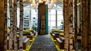 Un interno moderno con colonne in legno di betulla, un pilastro centrale con un volto e zone relax con cuscini gialli.