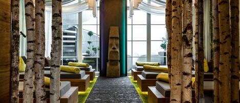 A modern interior with birch tree columns, a central pillar with a face, and seating areas with yellow cushions.