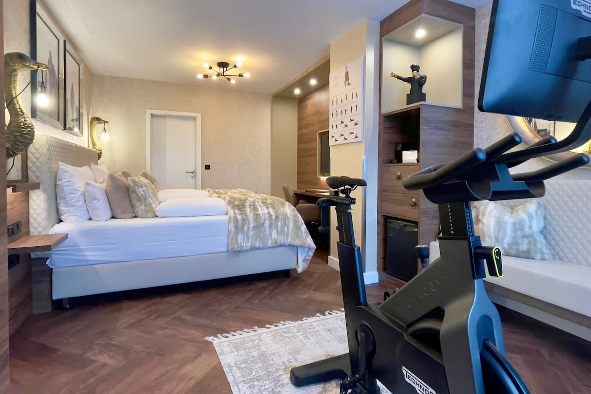 A modern bedroom with a bed, exercise bike, and a desk with a computer.