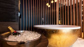 Ein modernes Badezimmer mit einer großen, goldenen Badewanne, einer Schale mit Eis und Champagner sowie einer Wandpaneele aus Holz mit vertikalen Lamellen.